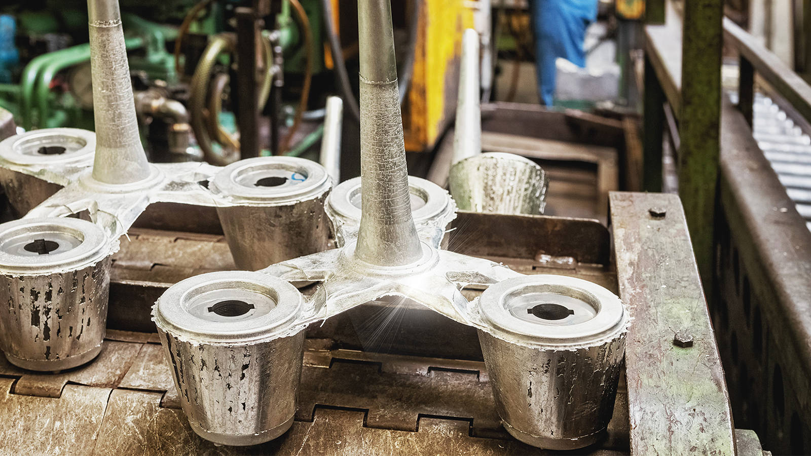 Pieces from die casting mold machine in a manufacturing facility with a worker in the background