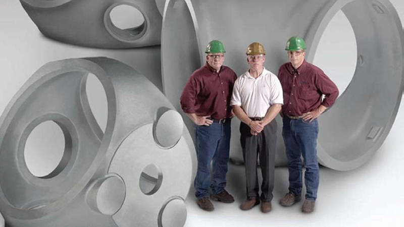Three workers at ATI Casting standing with three large wind turbine hubs