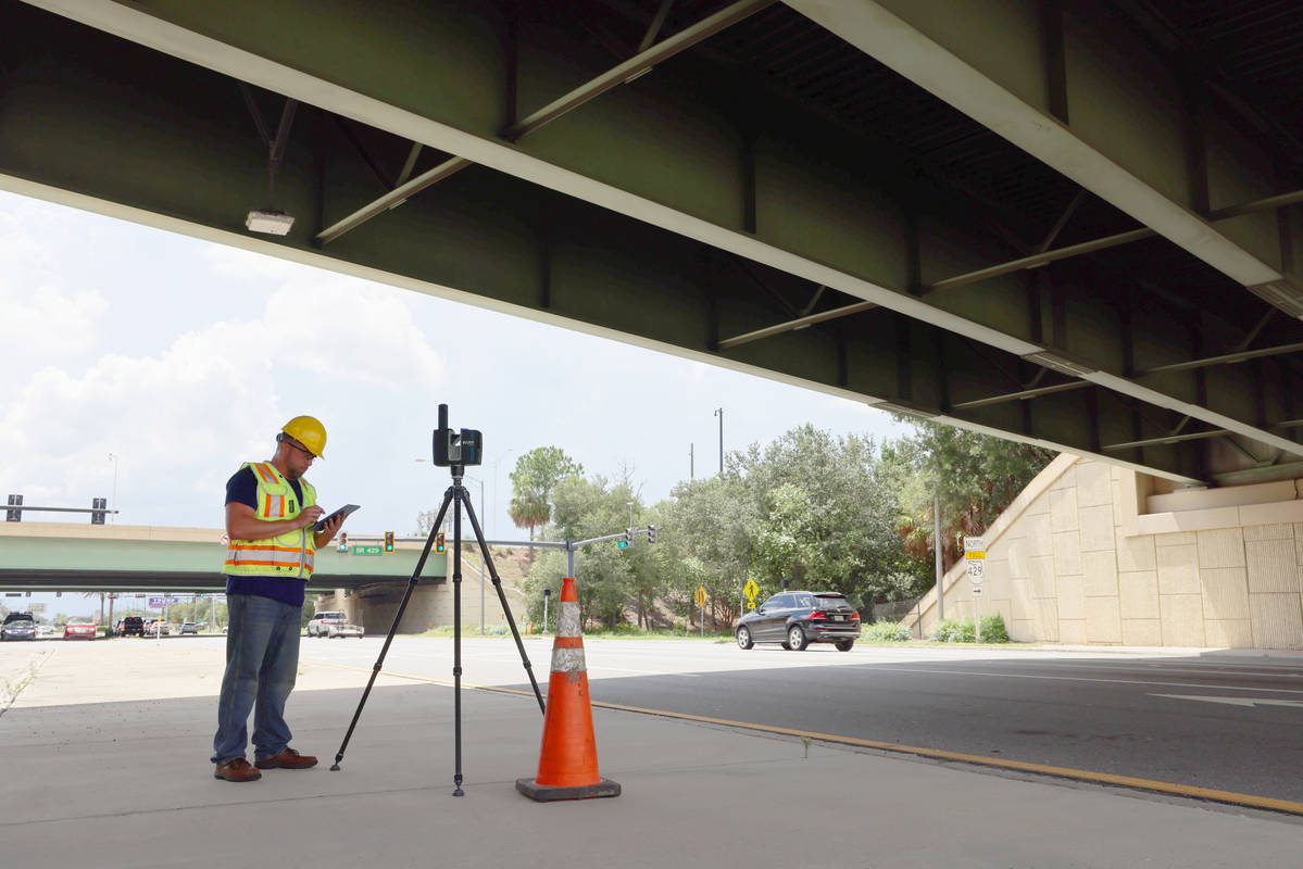 A man stood under a bridge in personal protection clothing with a tripod based terrestrial laser scanner