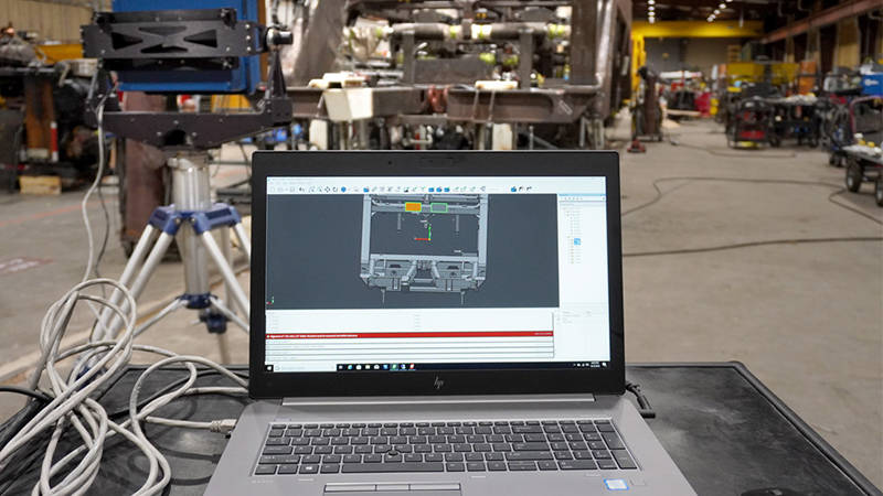 A parts assembly scan displayed on a laptop near assembly inspection equipment