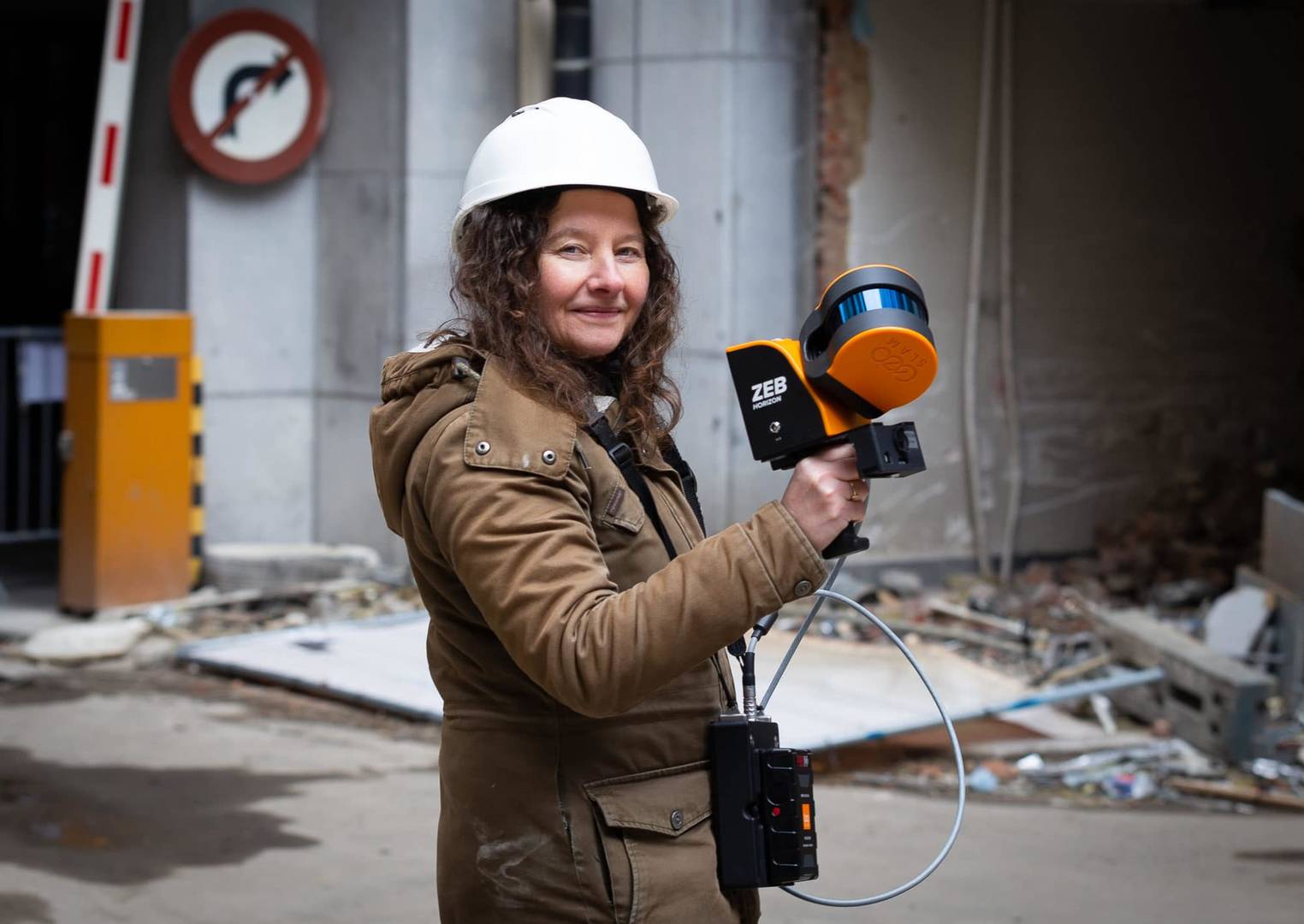 Lady posing with a mobile LiDAR scanner in front of a construction site