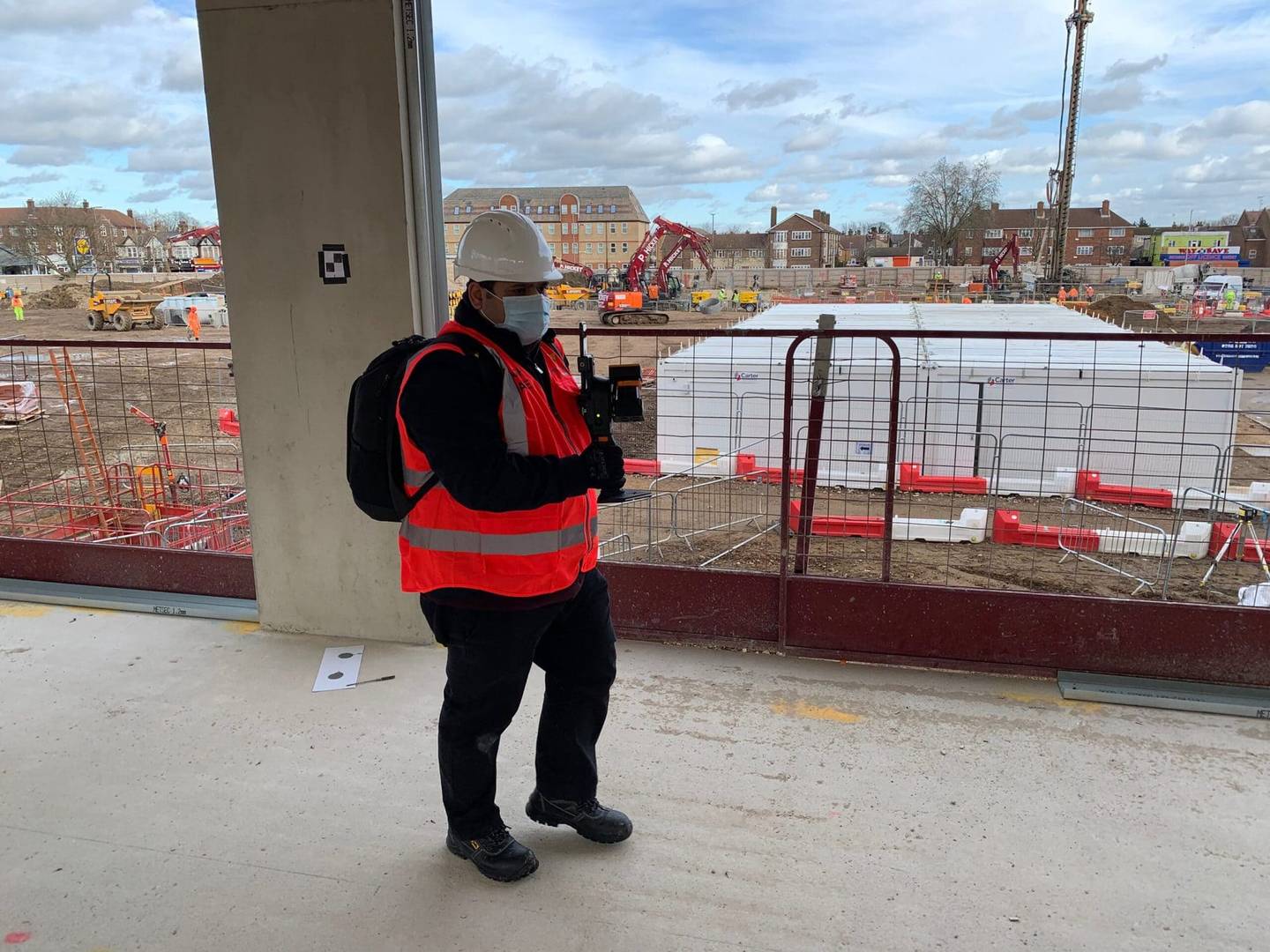 Man scanning a construction site with a mobile LiDAR scanner, wearing safety equipment