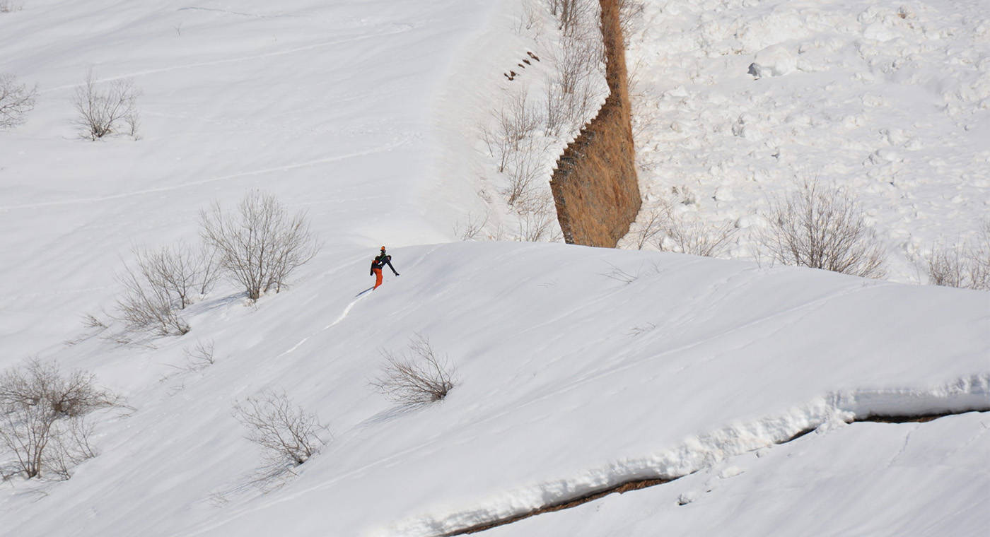 A vast snowy mountain range and a person in the distance scanning with a mobile LiDAR solution on a backpack