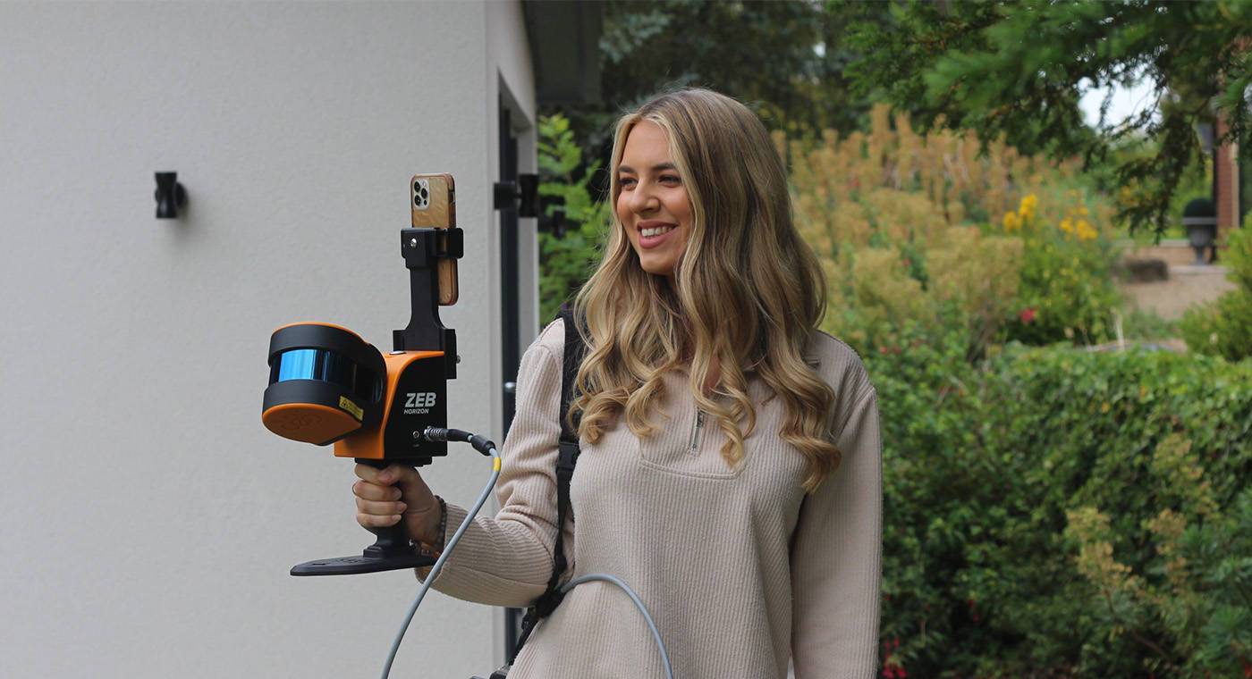 Blonde woman using a mobile LiDAR scanner in front of a house