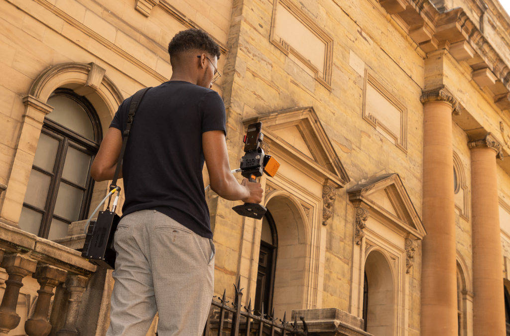 Person holding a mobile lidar scanner from behind walking down a street