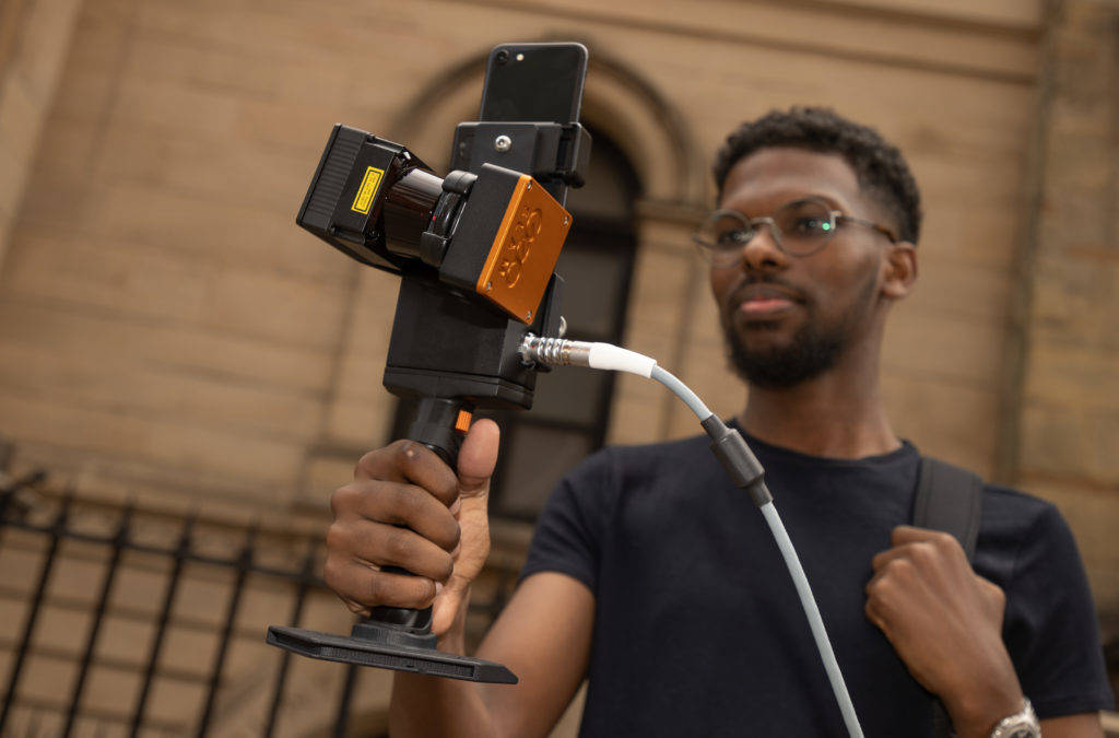 Person holding a mobile lidar scanner from the front walking down a street