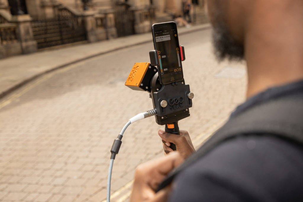 Person holding a mobile lidar scanner walking down a street