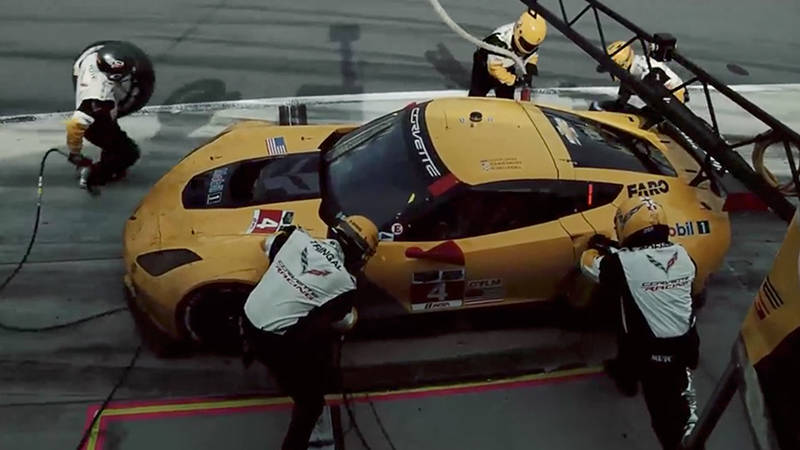 Five members of a pit crew checking a yellow Corvette